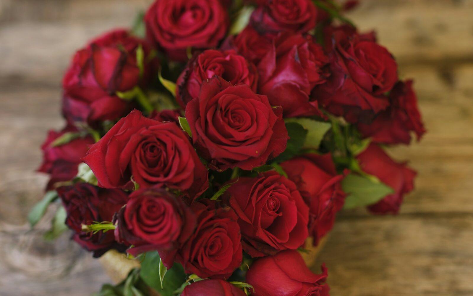 Two dozen red roses hand-tied on a wooden table, ready for same-day anniversary flower delivery from a Sedalia, MO florist