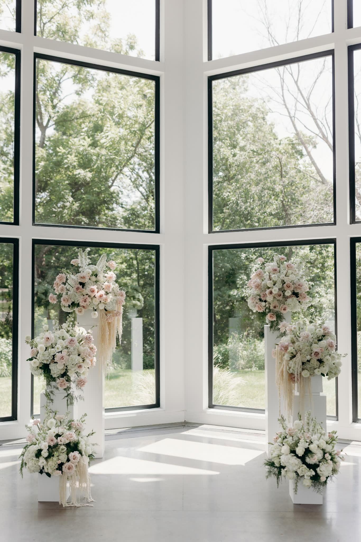 Symmetrical pedestal ceremony florals in blush and white framing tall windows