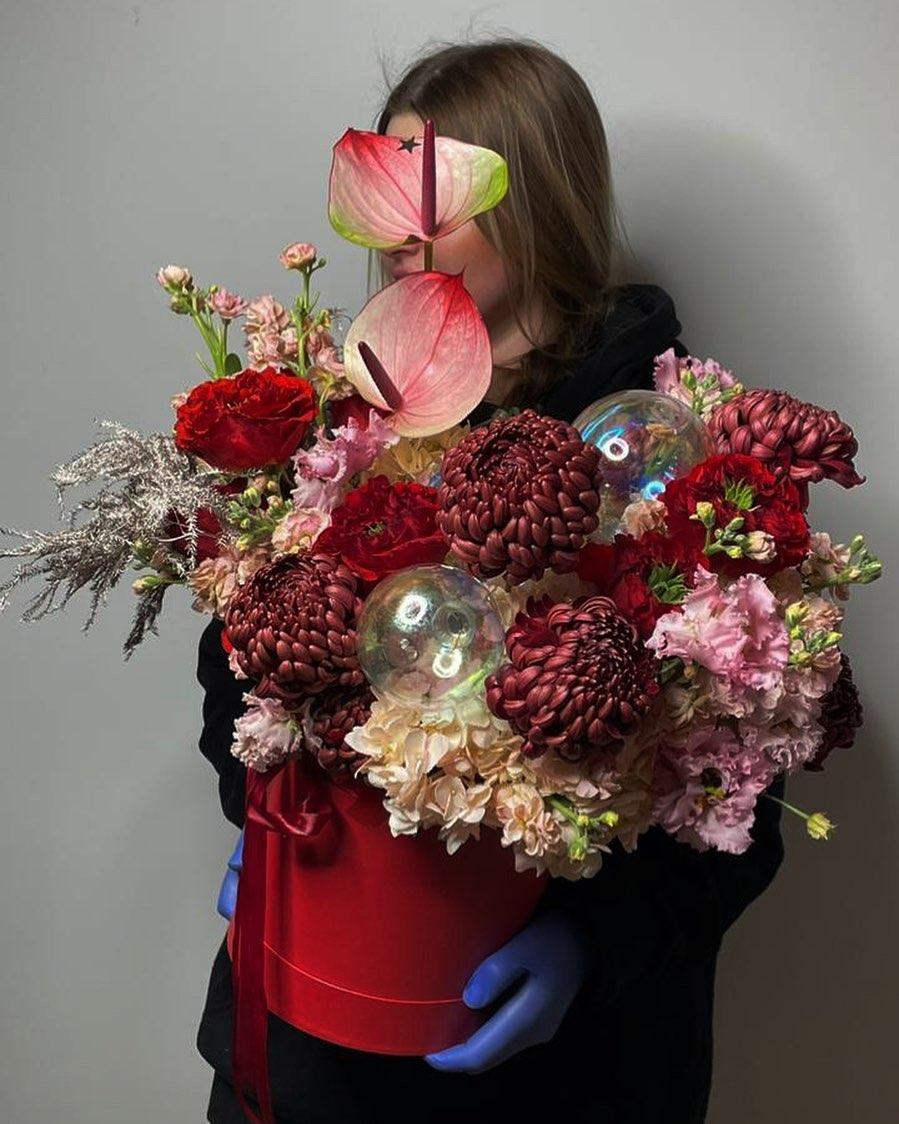 Deep red and pink holiday arrangement with anthuriums, burgundy chrysanthemums, glass orbs, and stock