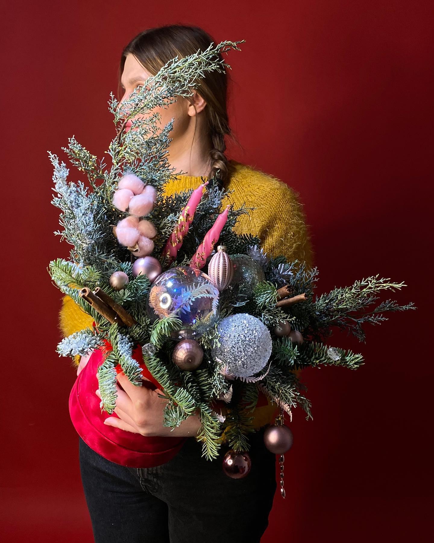 Festive Christmas bouquet with frosted evergreens, pink ornaments, cinnamon sticks, and cotton on red background