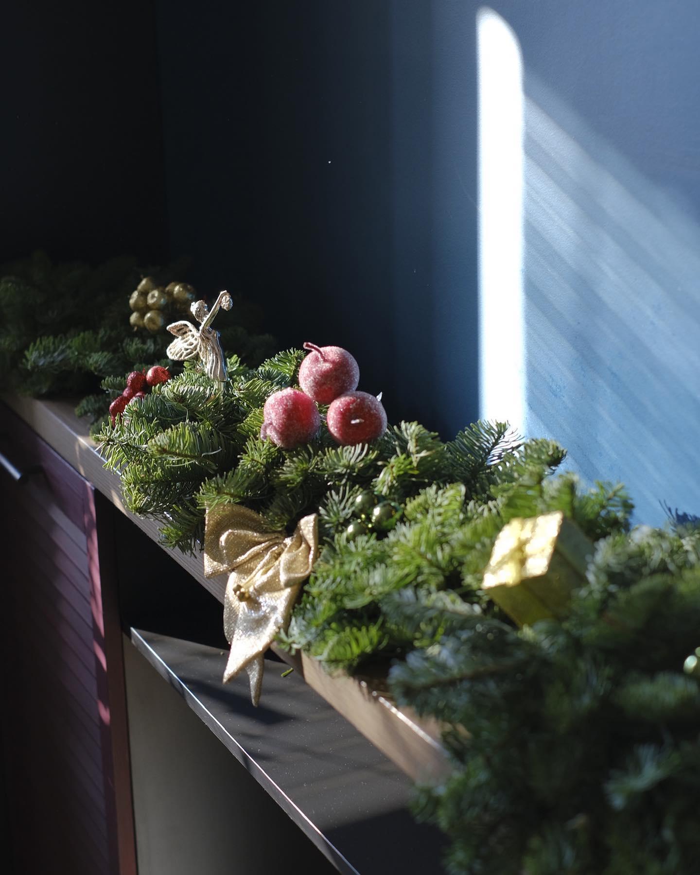 Holiday evergreen mantel display with angel figurine, gold bows, red berries, and frosted apples