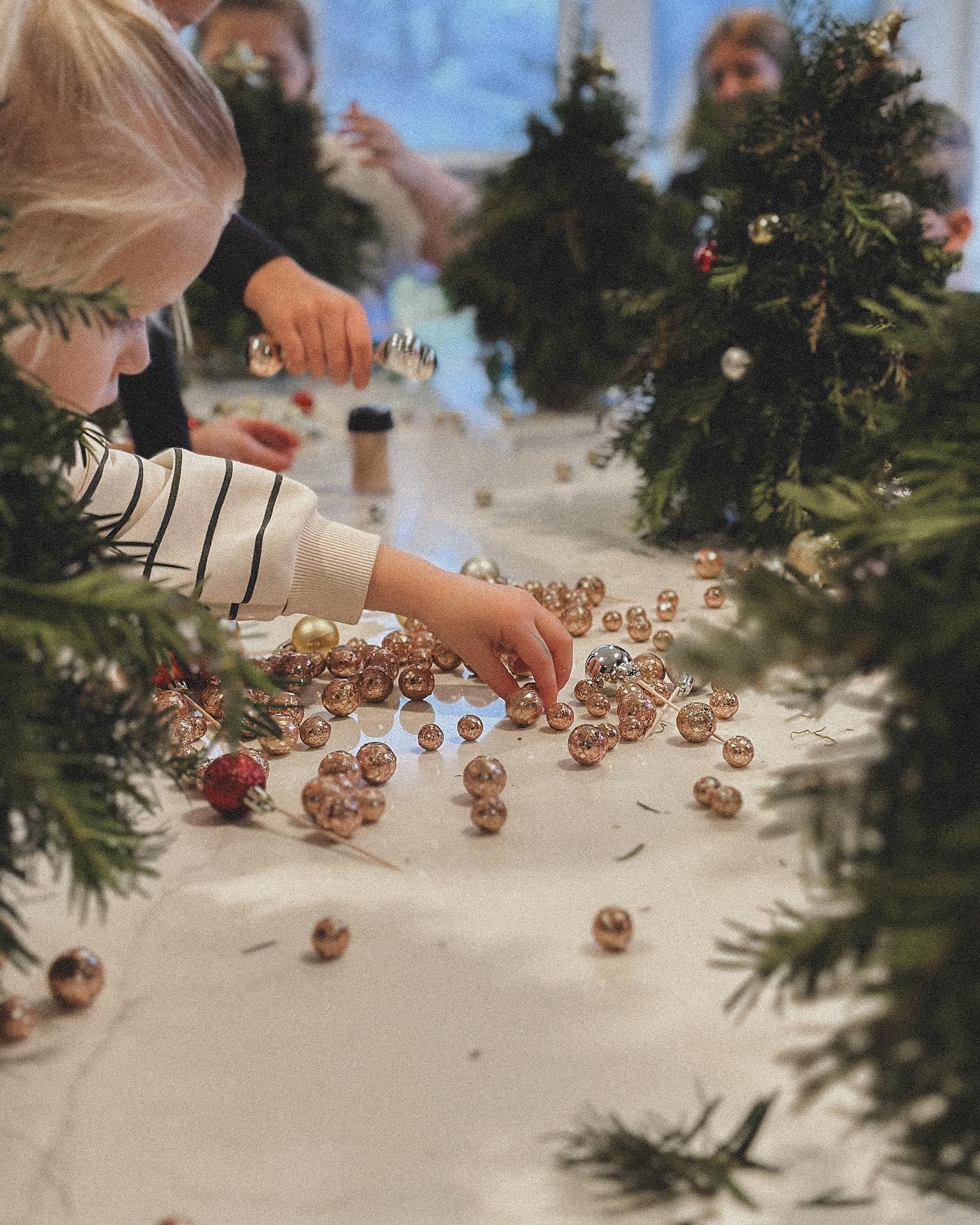 Children decorating evergreen Christmas wreaths at floral workshop with ornaments and baubles