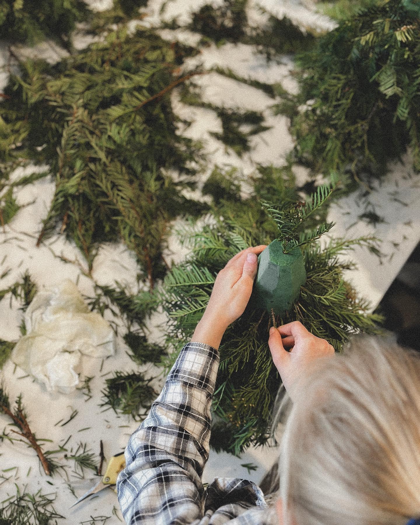 Young girl carefully placing baubles on handmade evergreen wreath at holiday floral class