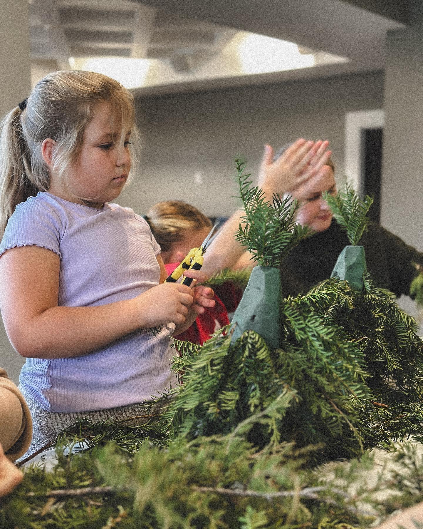 Children learning to arrange fresh greenery and holiday decorations at hands-on floral workshop