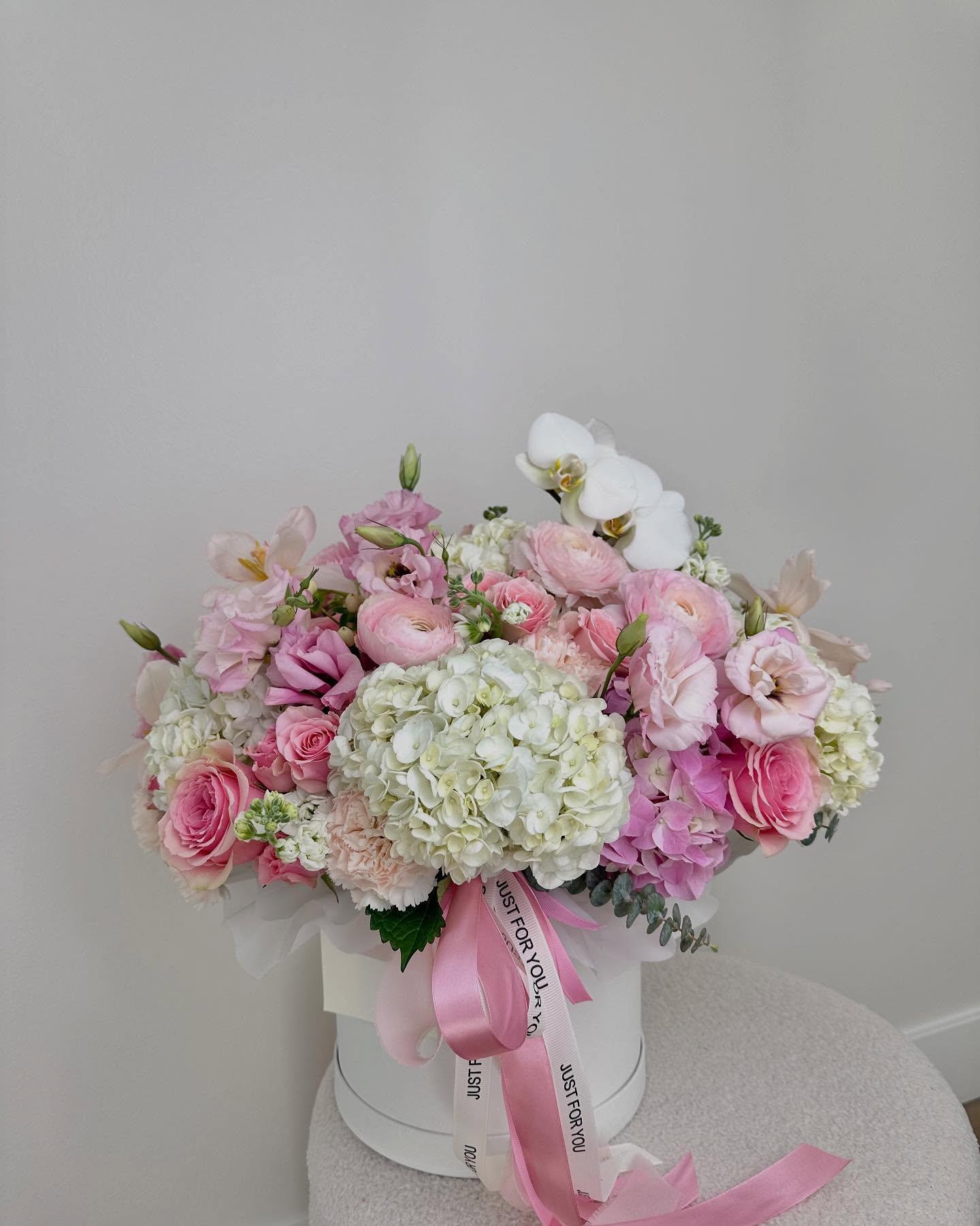 Pink and white hat box arrangement with ranunculus, hydrangea, orchids, and "Just For You" ribbon