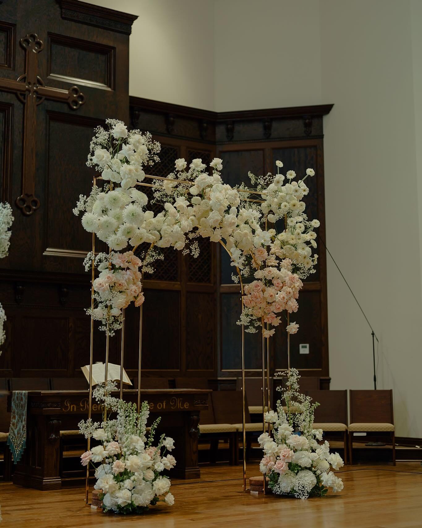 White and blush wedding ceremony arch with roses and dahlias on gold frame in church sanctuary