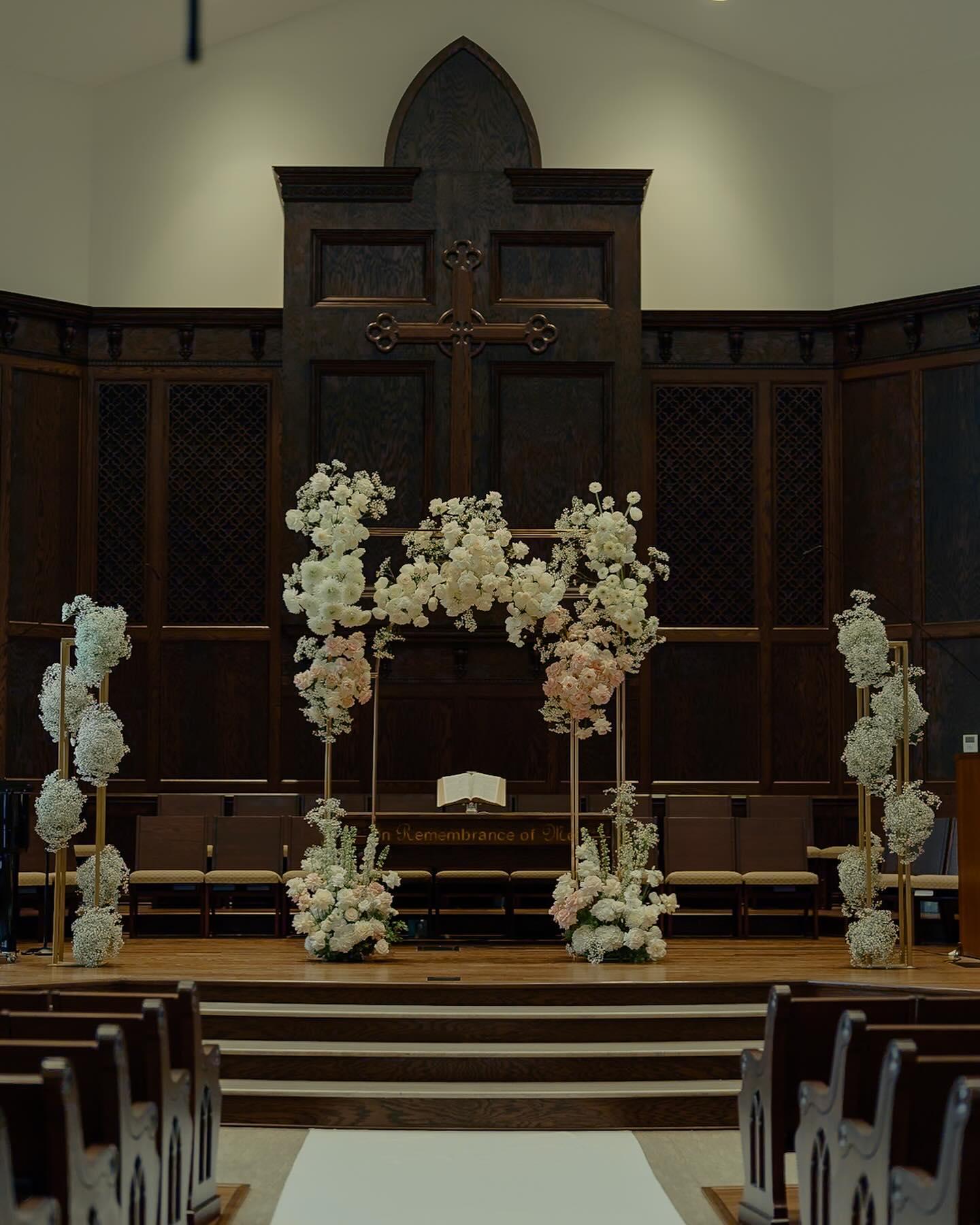 Church wedding ceremony from pews showing full floral arch with white draping and baby's breath columns
