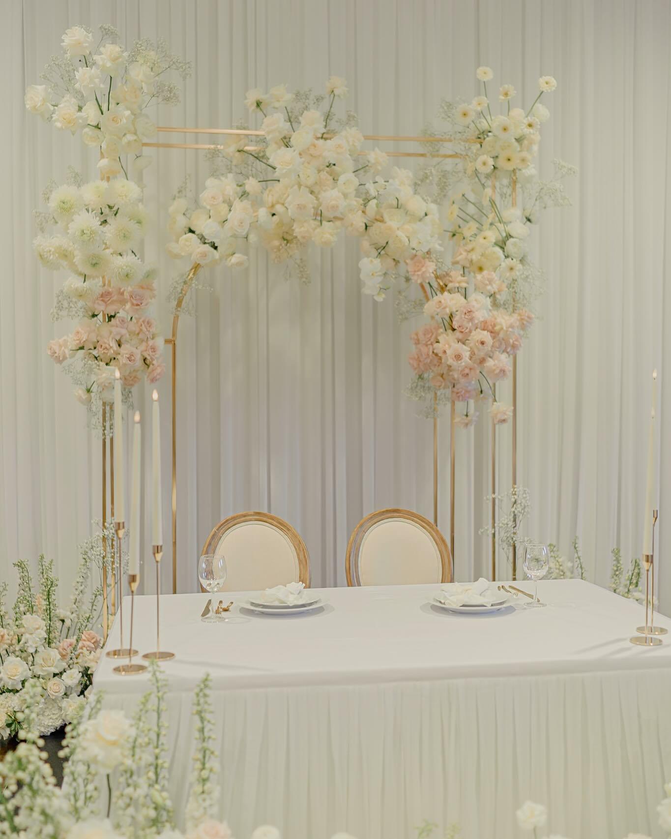 Close-up of white and blush sweetheart table backdrop with gold frame, roses, dahlias, and baby's breath