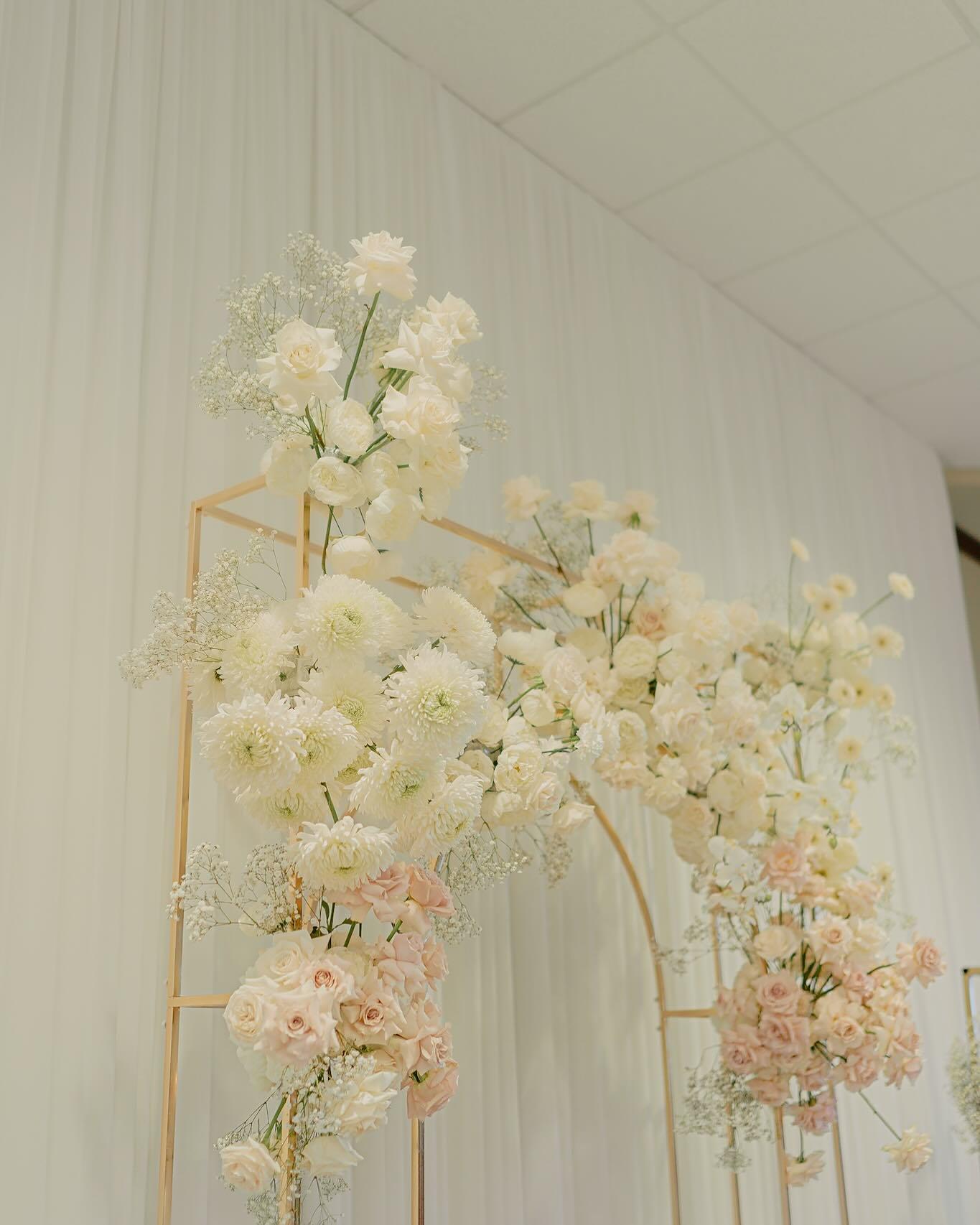 Detail shot of gold arch with cascading white dahlias, blush roses, and baby's breath for wedding backdrop